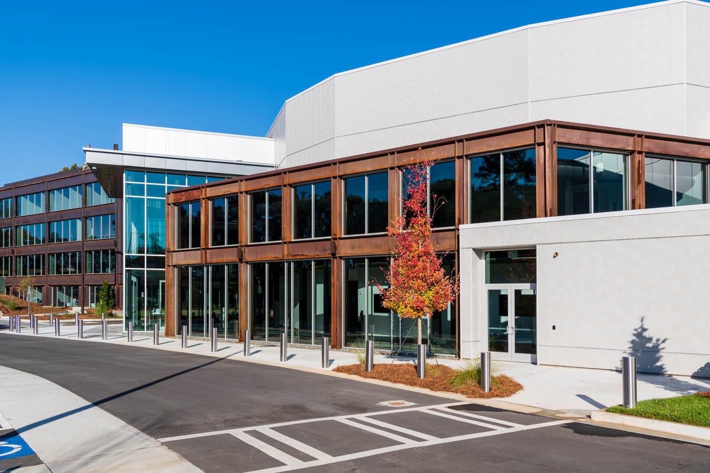 Passion City Church at Cumberland - Phase I: Modern office building with glass facades and a single red-leaved tree in front, under a clear blue sky.