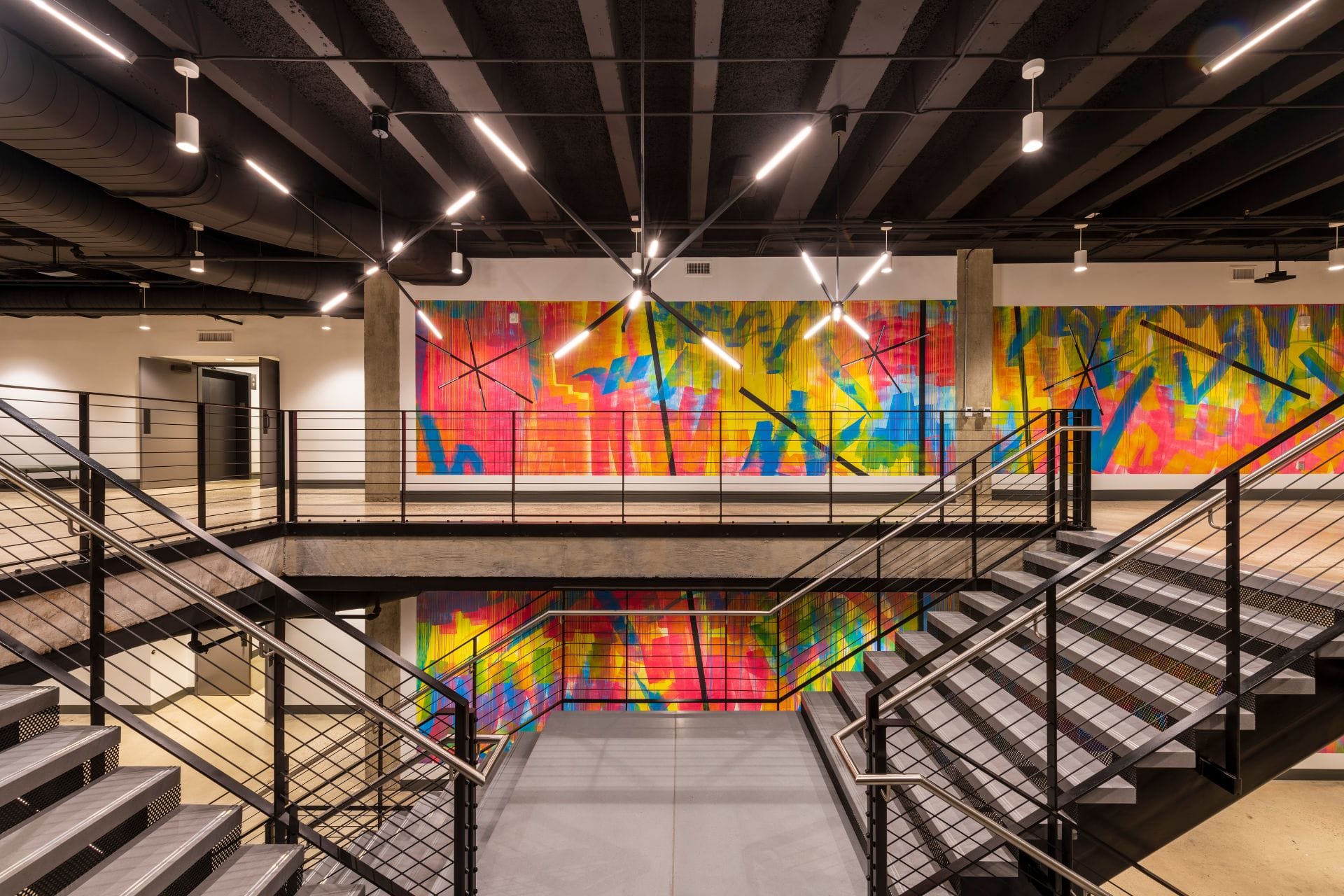 Modern staircase with metal railings in an open, brightly lit home. Colorful abstract mural on the far wall.