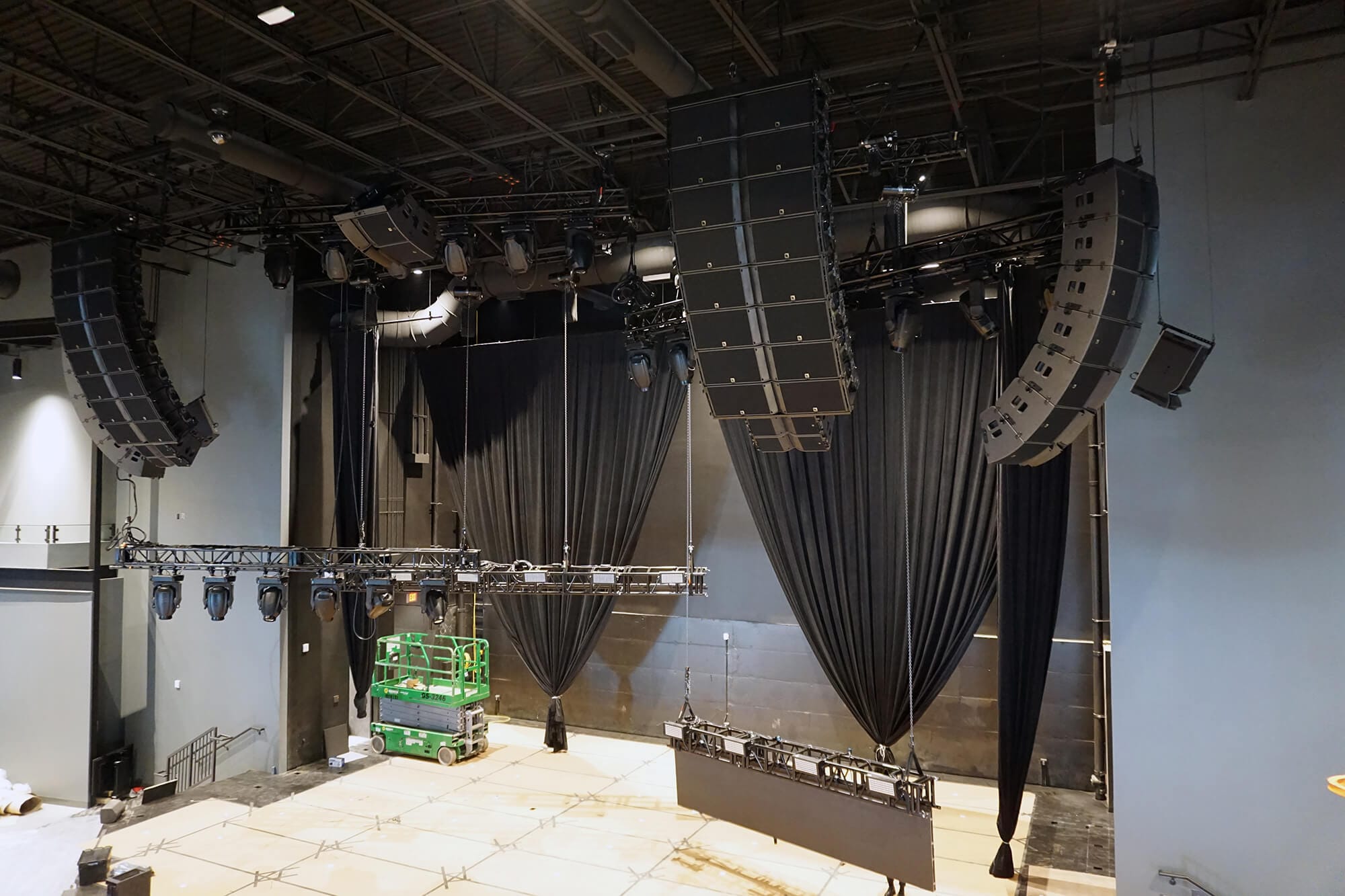 Empty stage setup with black curtains and overhead lighting equipment, large speakers hanging, and a green lift positioned near the back wall, reminiscent of Phase I at Passion City Church in Cumberland.