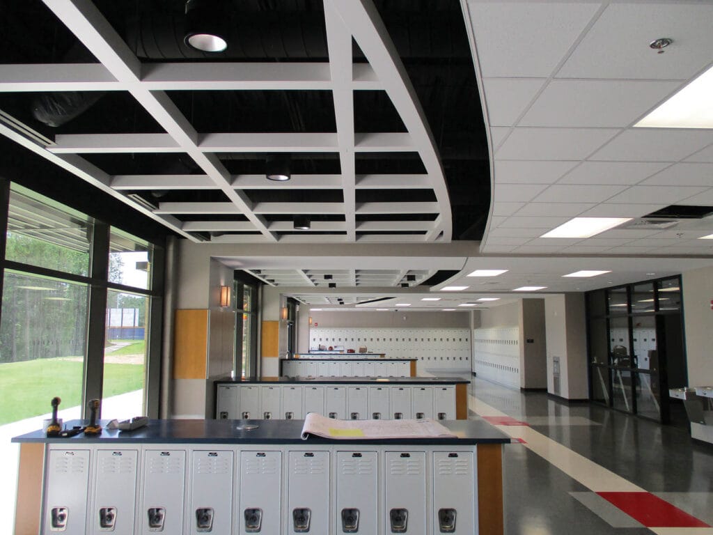 A modern school hallway with rows of white lockers, large windows, and a grid ceiling design.