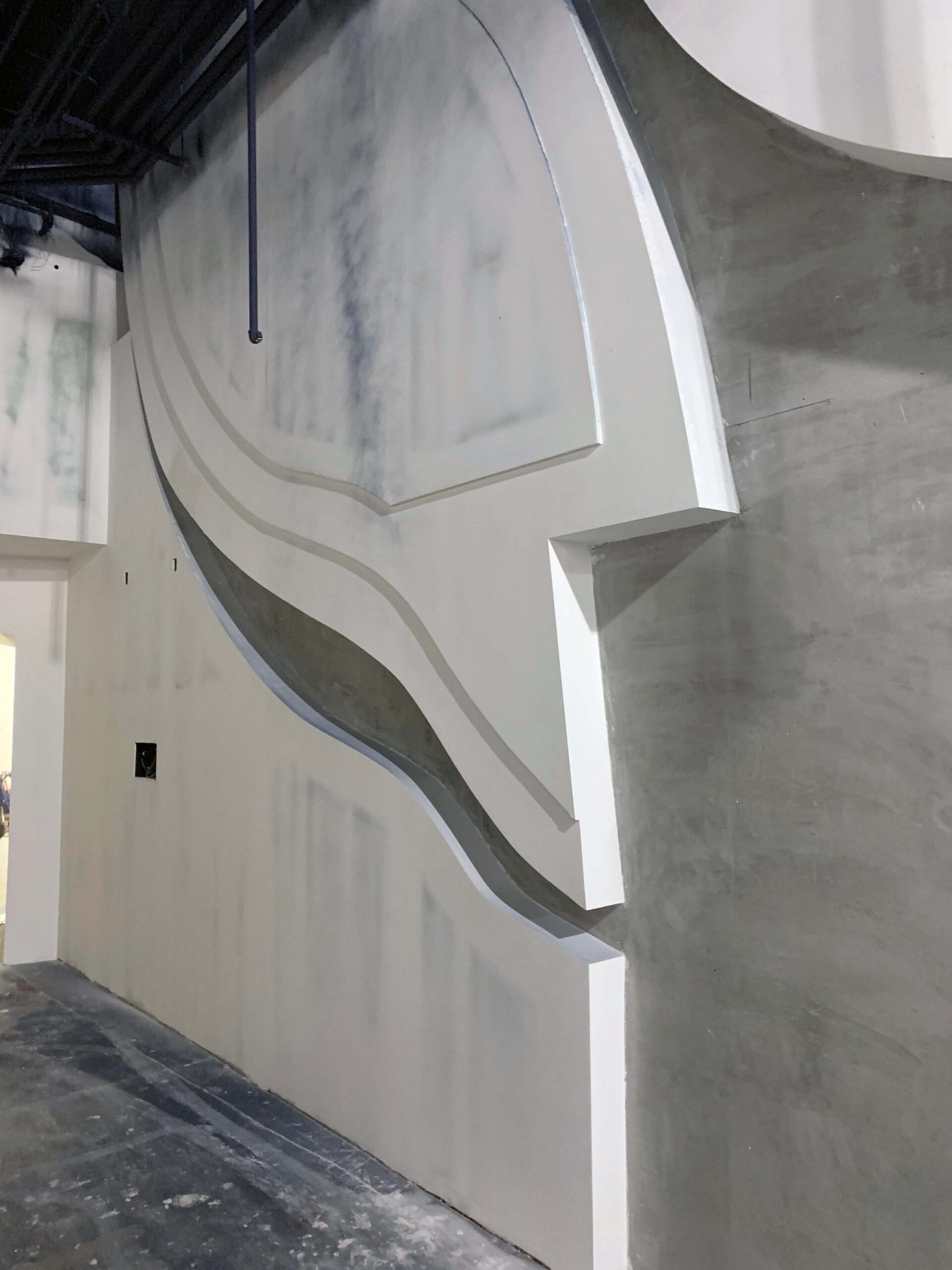 A large wall with abstract, geometric shapes and patterns carved into it, reminiscent of the fluidity found at an aquarium, partially painted white.