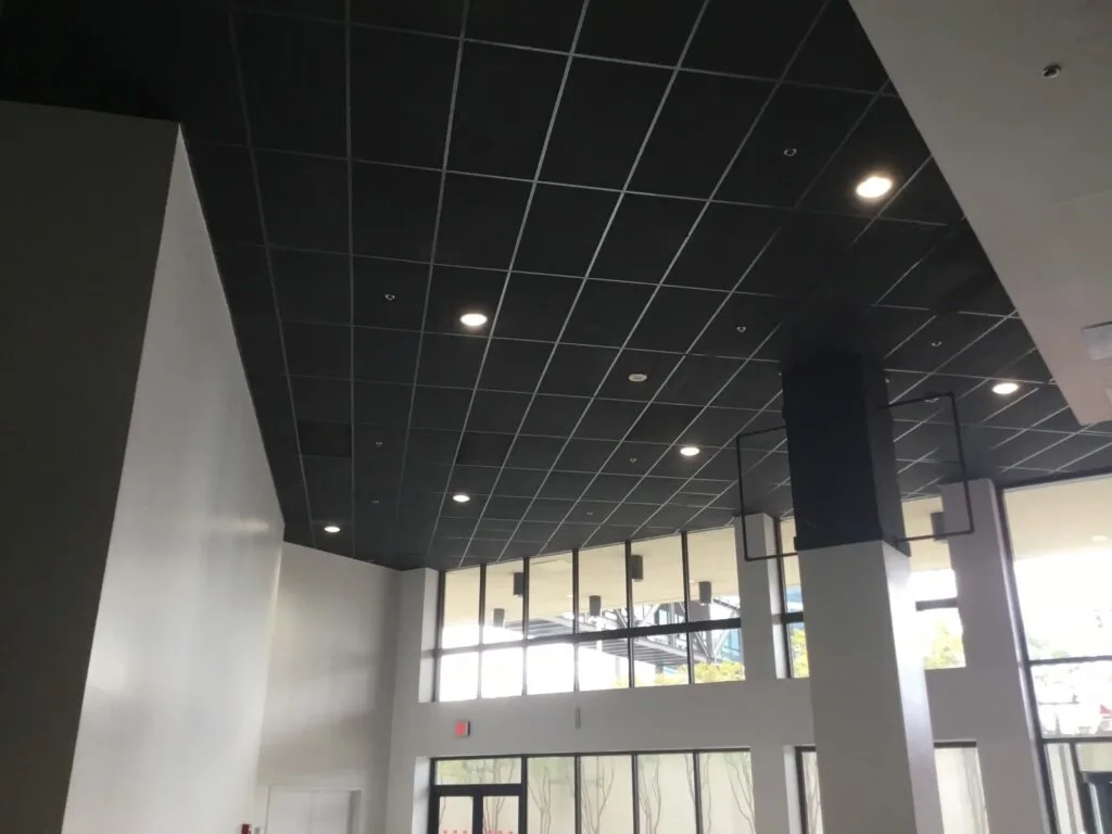 Interior view of a tall room with a dark grid-patterned ceiling, recessed lighting, and large windows, showcasing the sleek design typical of modern commercial construction.