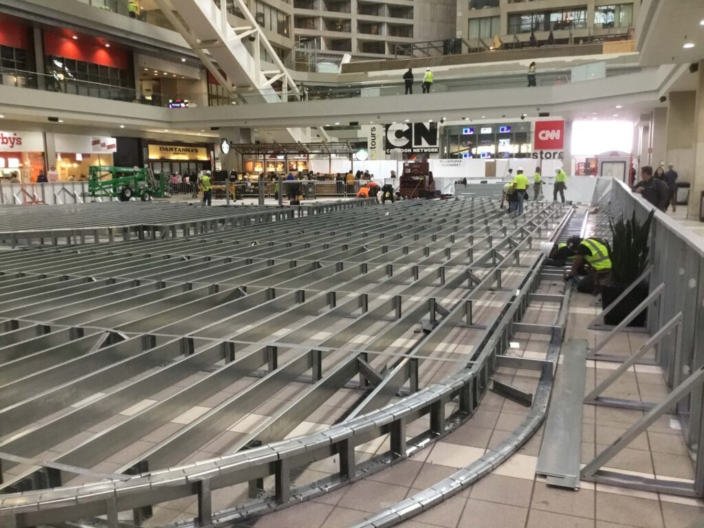 Construction workers expertly assembling a large metal framework inside a bustling shopping mall, showcasing the precision and skill of commercial construction.