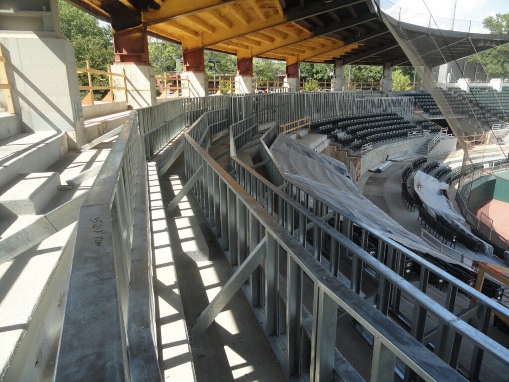 The view showcases a partially constructed stadium, where metal framing elegantly supports exposed beams and rows of seating beneath a sleek metal roof.