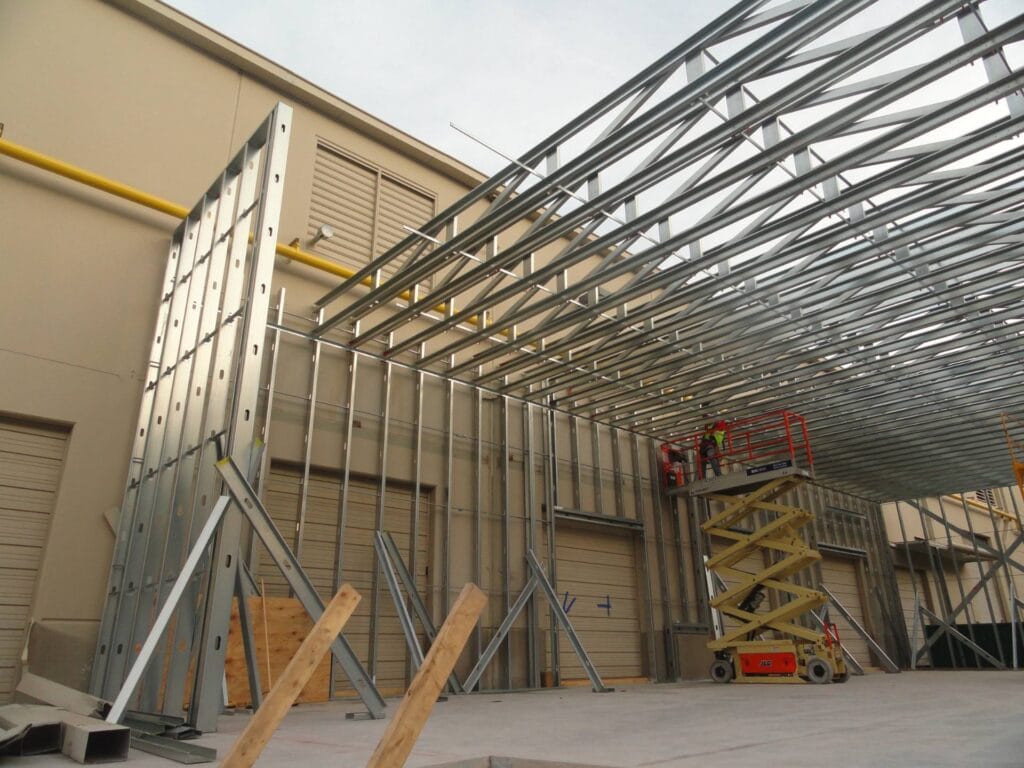 Construction site with metal framing and scaffolding. Workers on a lift install metal beams on a building exterior.