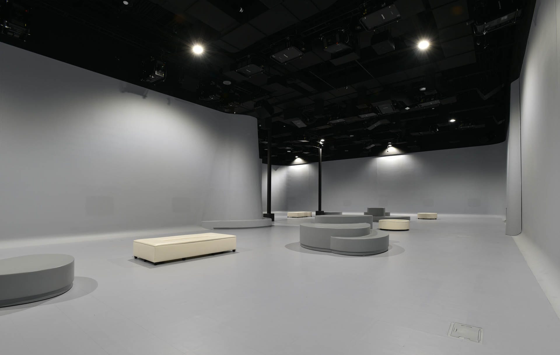 The empty gallery space boasts a minimalist design, with a gray floor and curved light gray walls. Scattered low, circular platforms add interest, while ceiling lights transform the area into an illuminarium of creativity and inspiration.