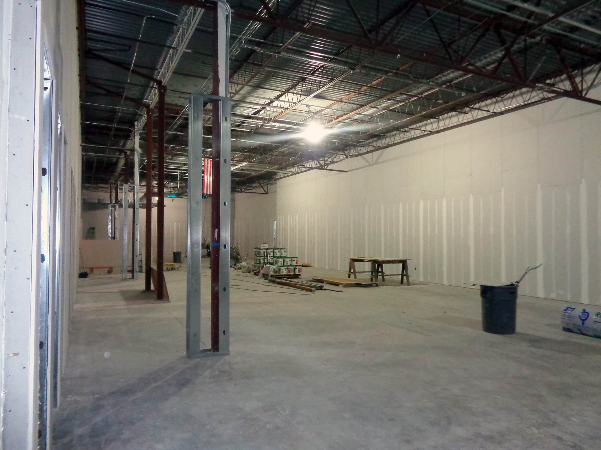 The interior of a large, unfinished warehouse—dubbed Project-ATL4—features exposed metal beams and partial drywall. A workbench, construction materials, and tools crucial for this mission-critical build are scattered on the concrete floor.
