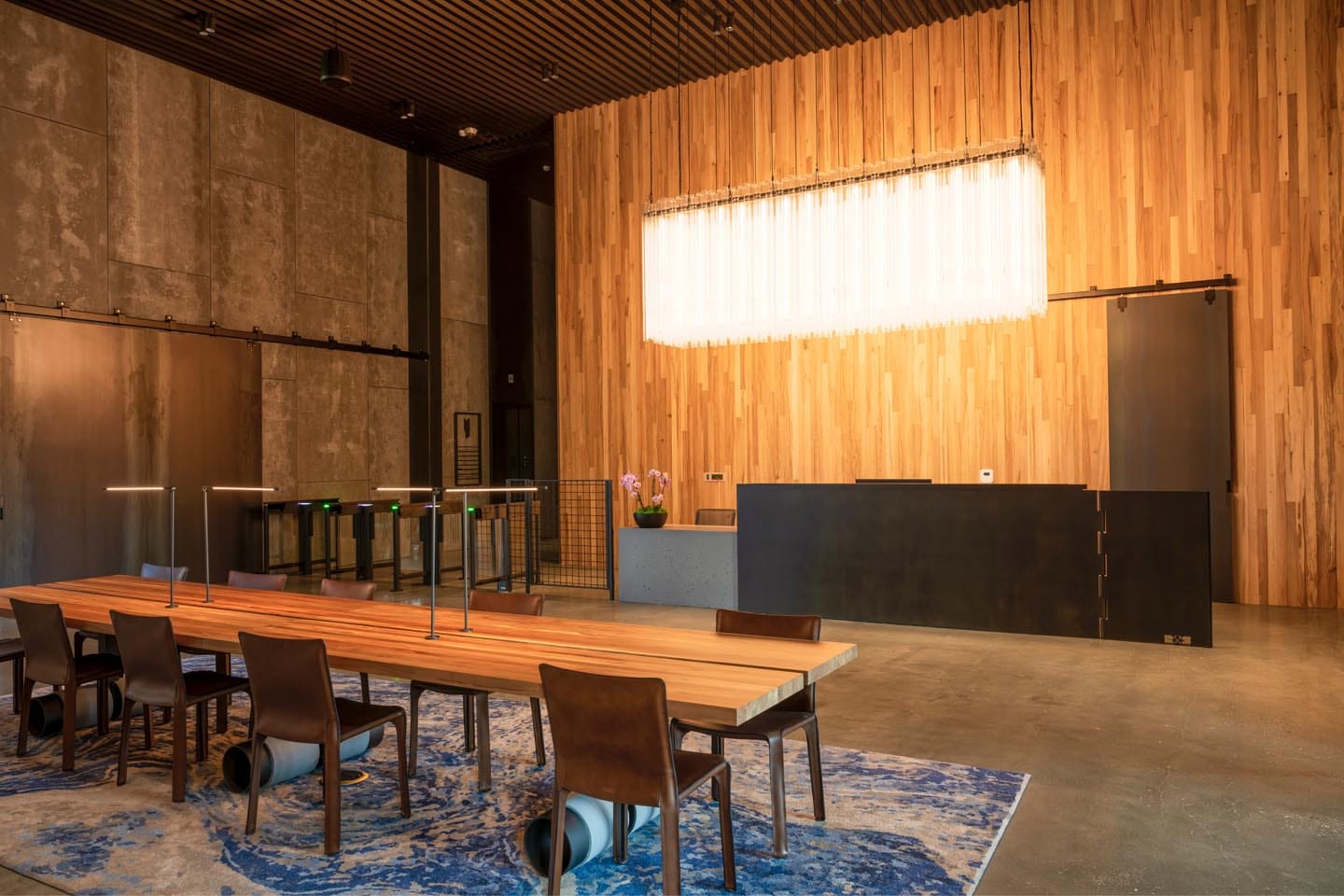 About Us 5 Modern office lobby with a wooden reception desk, long communal table with chairs, overhead lighting, and concrete flooring—reflecting the collaborative spirit found in our About Us story.
