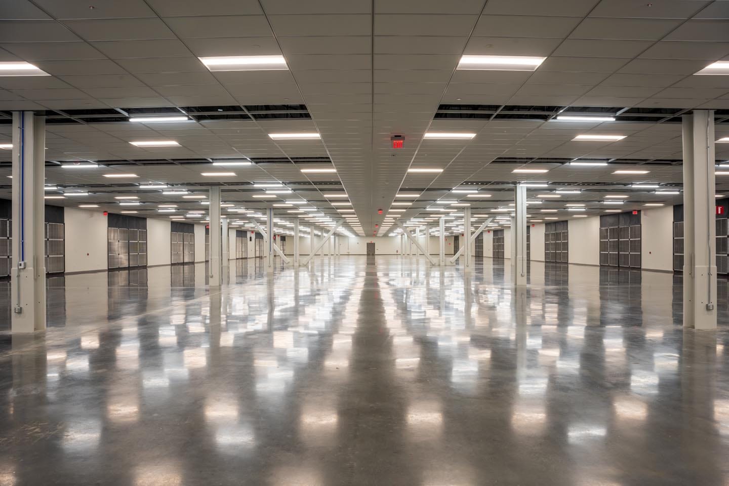 About Us 4 A large, empty industrial warehouse with polished floors, white pillars, and overhead fluorescent lighting stretching into the distance sets the stage for our story—learn more in our About Us section.