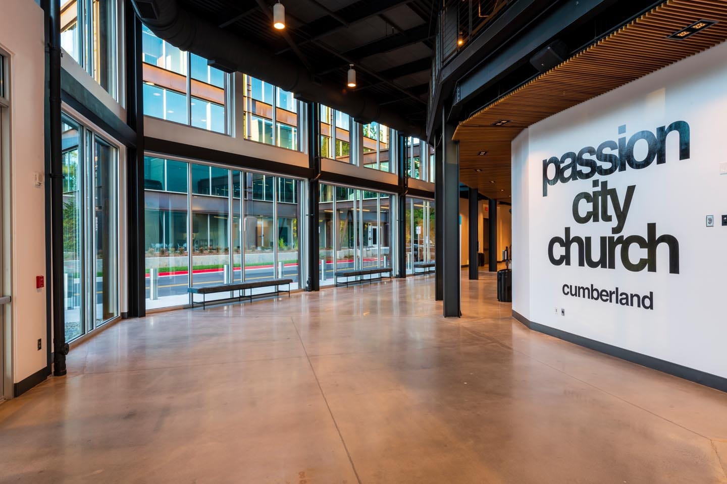 About Us 3 Spacious modern lobby with large windows and an “about us” display beside the “Passion City Church Cumberland” sign on a white interior wall.